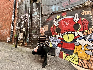 Cover image for 'Is Ann Arbor Worth Visiting' of travel blogger Michael DeFranceschi kneeling in front of am mural in downtown Ann Arbor, MI
